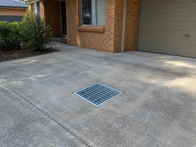 Clean outdoor drain grate set in a concrete driveway beside a brick house in South Penrith