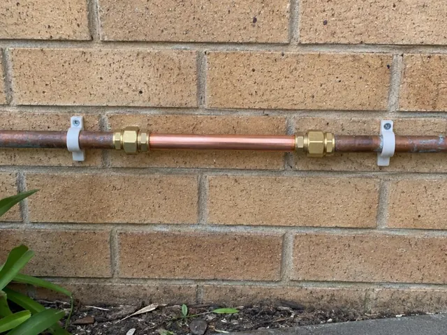 Repaired copper water pipe on an exterior brick wall with brass couplings in Cranebrook